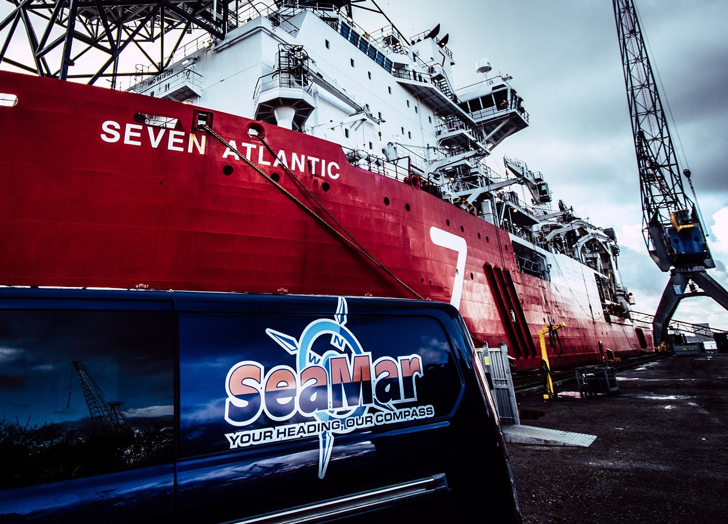 A SeaMar van in the harbor with the ship "Seven Atlantic" and a crane in the background