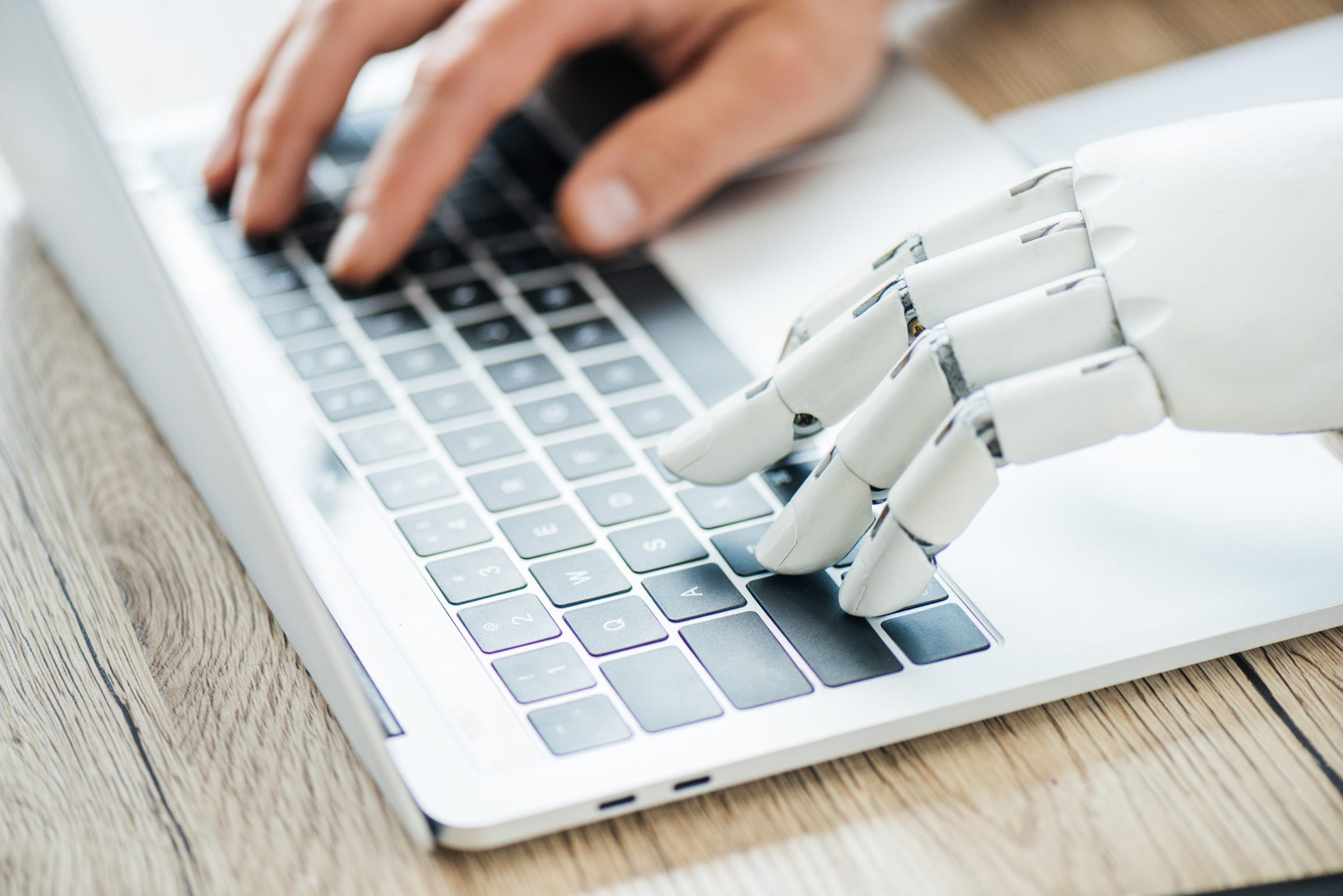 Menschenhand und Roboterhand bedienen gemeinsam die Tastatur eines Laptops